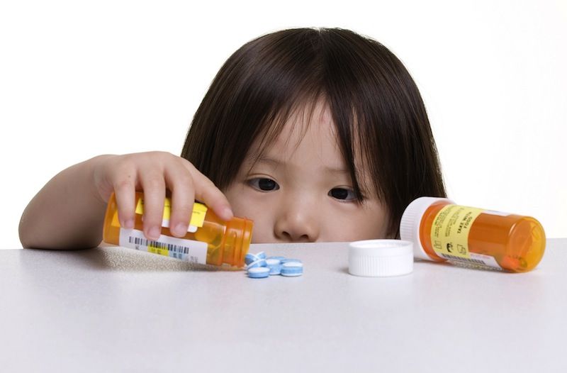 A little girl looks at blue pills on a counter.