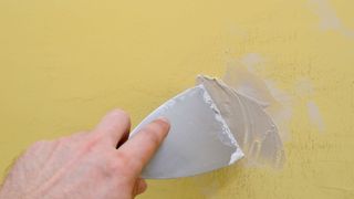 Man filling in a crack on a yellow wall