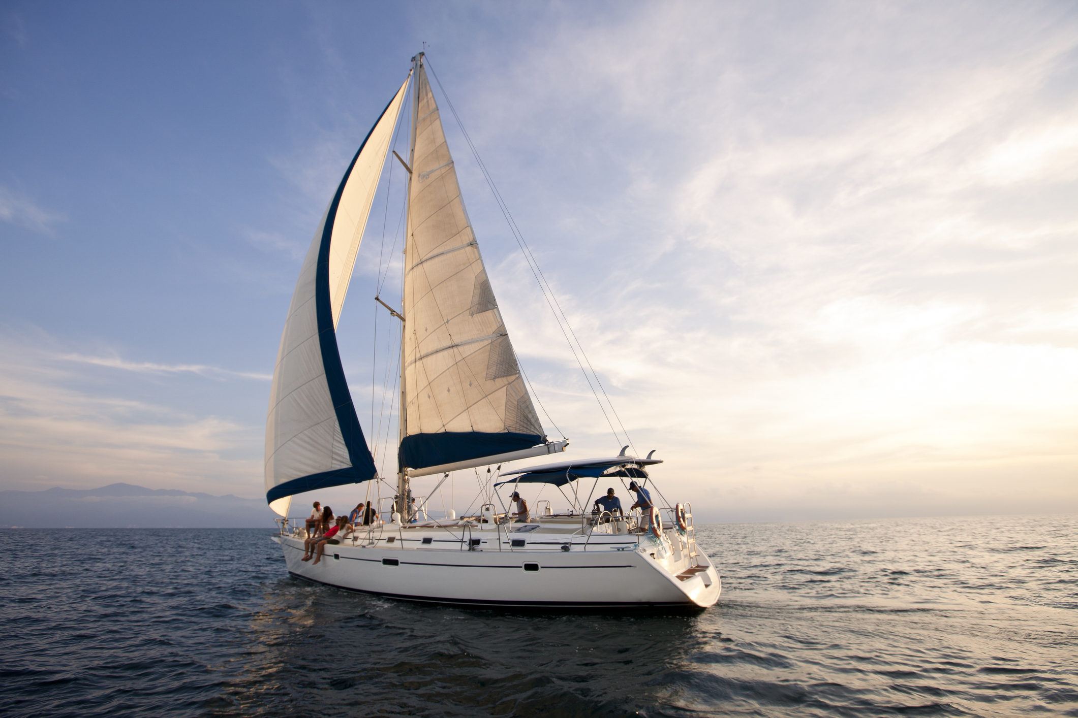 Multiple people enjoy a smooth boat with high sails on a calm day on the water.