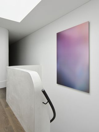 Image of an all-white hallway and staircase with black railing. There is an abstract painting in a cosmic colorway hanging on the wall