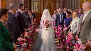 Ziva David walking down church aisle for faux wedding wearing bridal dress and veil, while people on either side of her are standing and watching
