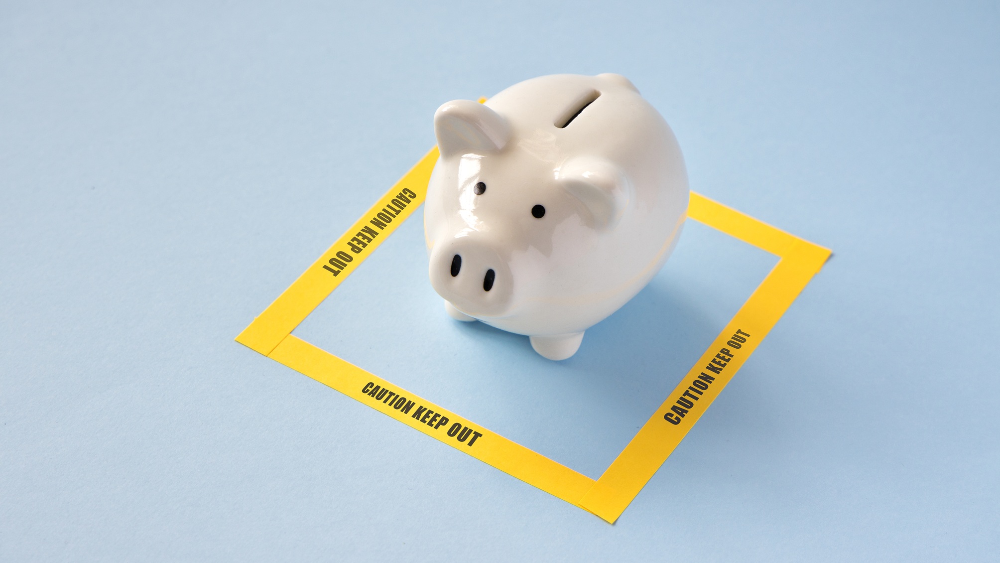 A white piggy bank surrounded by caution tape against a blue background.