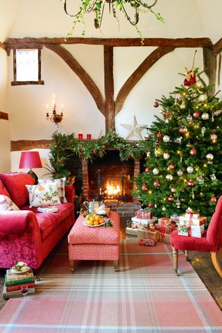 A traditional red and green Christmas-themed living room with large decorated Christmas tree, check rug and red sofa furniture