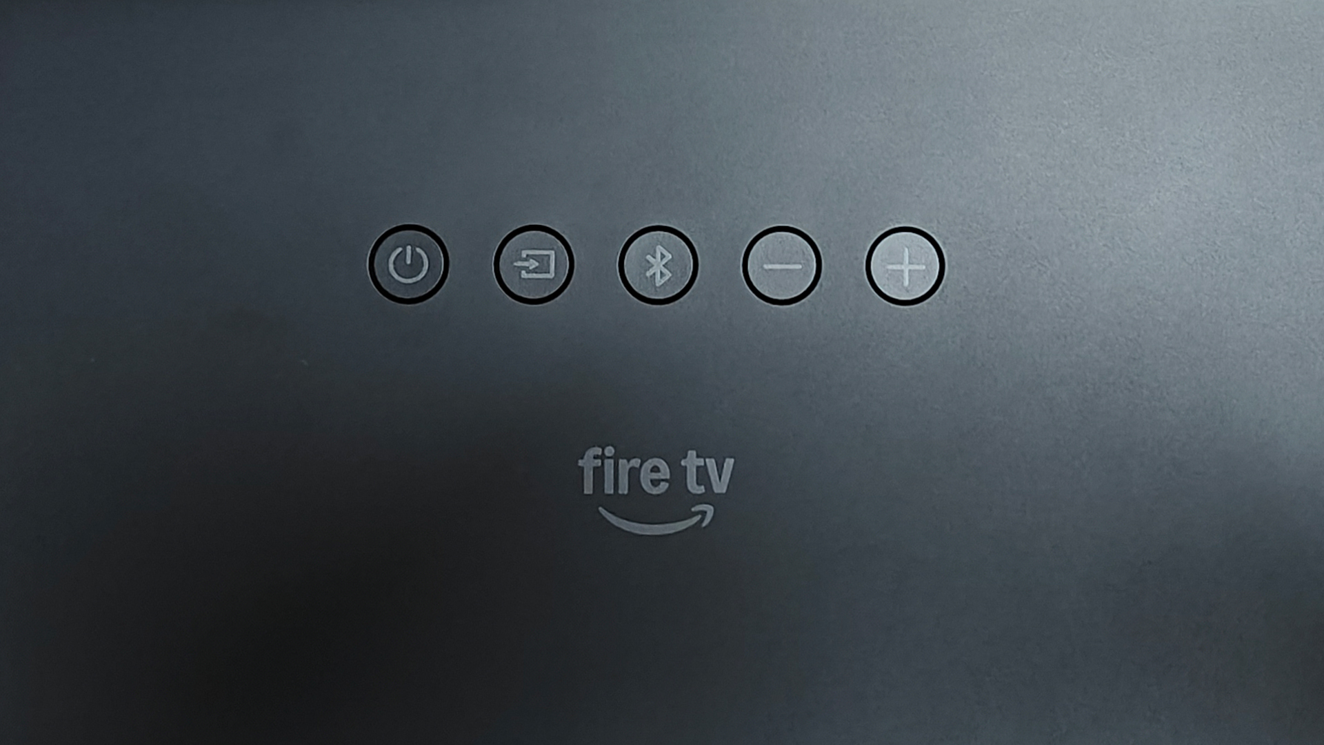 Amazon Fire TV Soundbar Plus Dolby Atmos soundbar close up on Fire TV logo and control buttons on top of unit