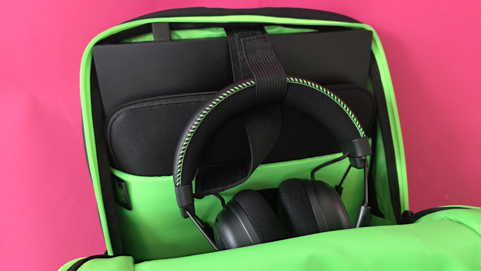 A black Razer backpack containing Razer headphones and two laptops
