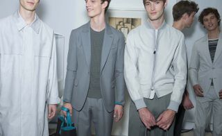 Three male models wearing clothing by Berluti in light grey shades.