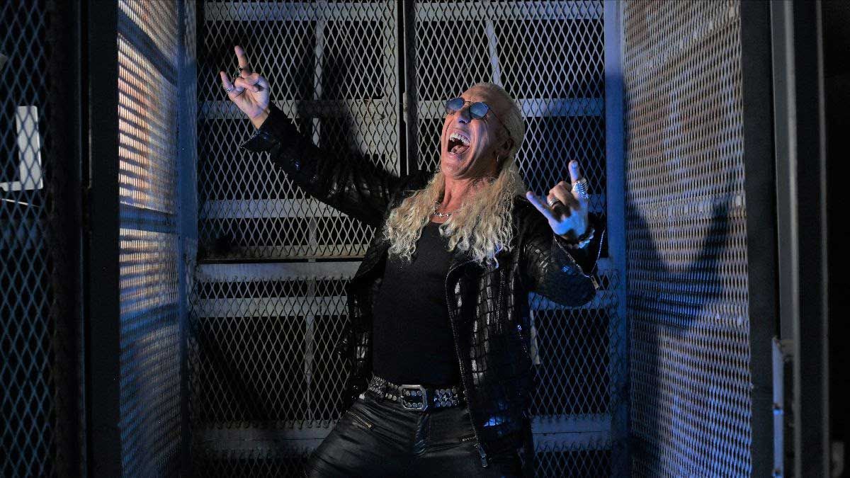 Dee Snider prentending tio scream while throwing the horns in a warehouse