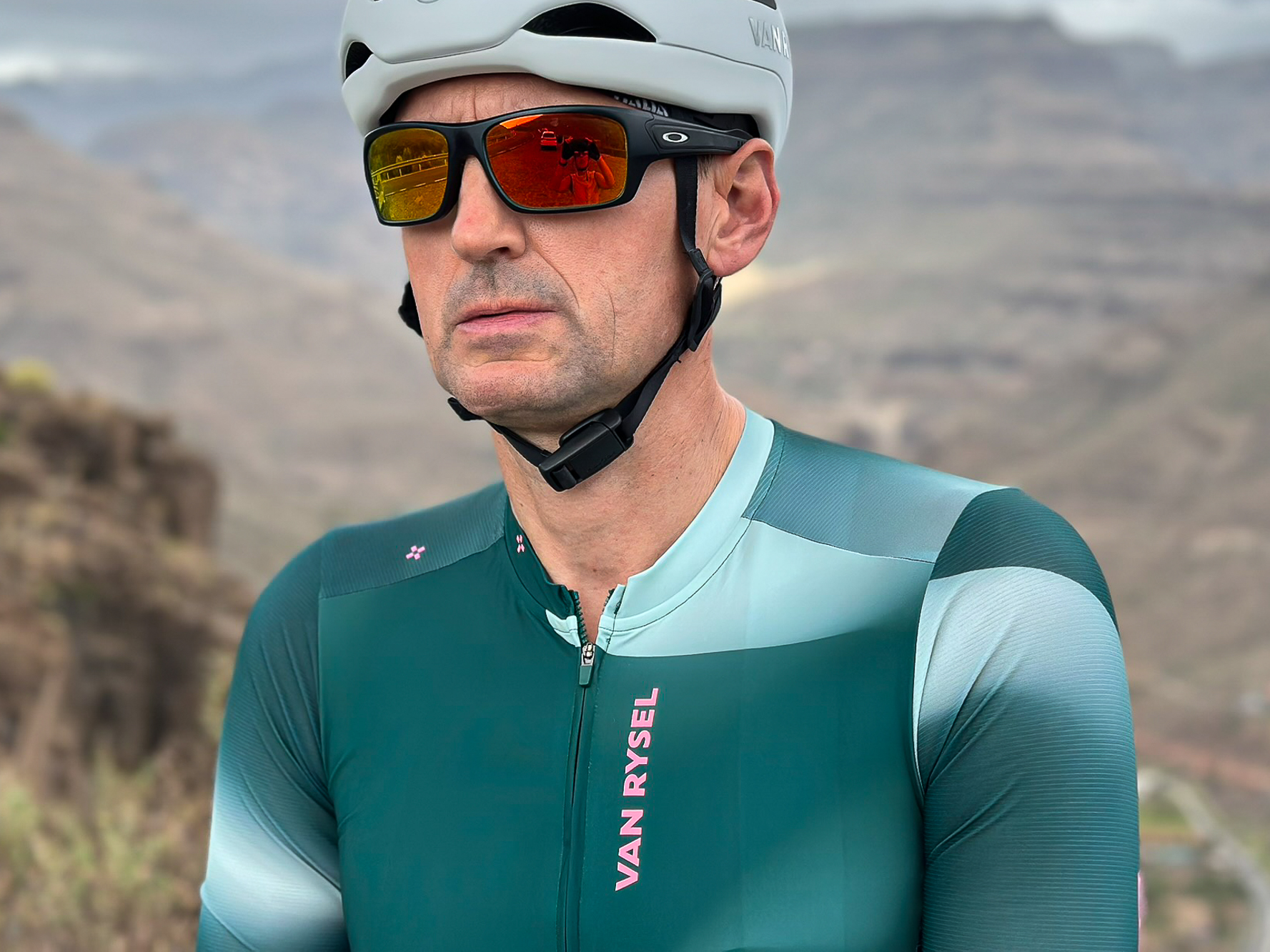 close up of a man wearing a green jersey, white helmet and black sunglasses