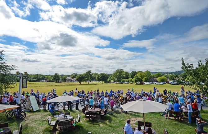 View over Abinger Hammer cricket ground as the peloton ride by fans in the Surrey countryside sitting in their local watering hole
