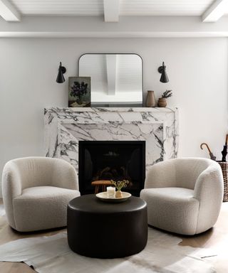 Black and white living room with two matching armchairs and black coffee table, situated around a marble fireplace, mirror on mantel, two matching wall lights, animal skin style rug