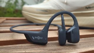 Shokz OpenRun Pro 2 in-ear headphones on wooden garden table in front of running shoe