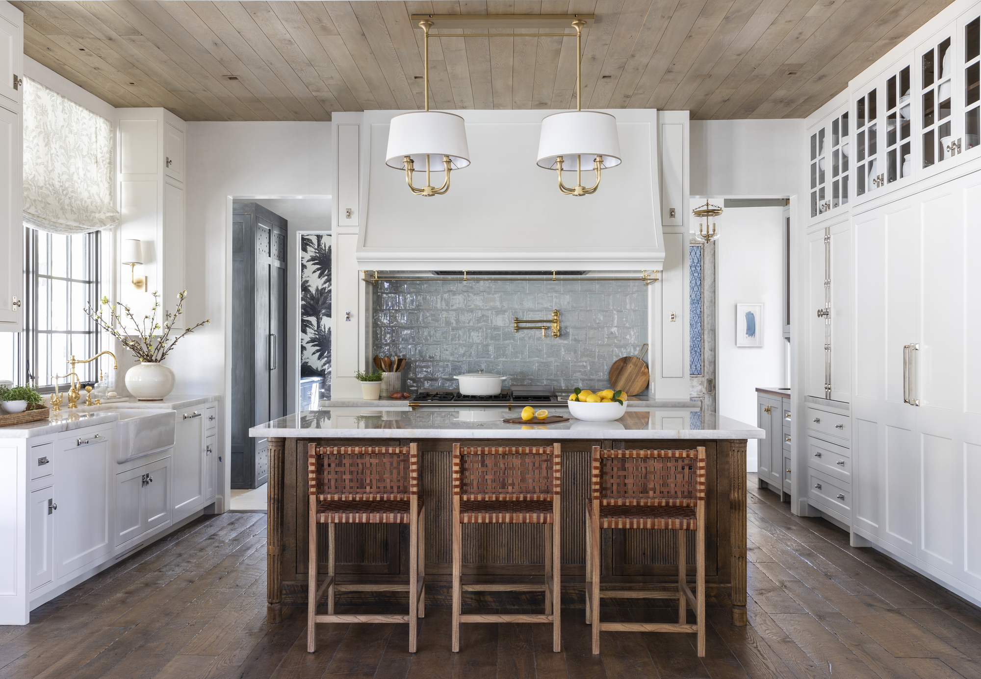A kitchen with white cabinetry, an island, and a range alcove with light blue zellige tiles and a pot filler tap