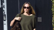 Margot Robbie wearing an olive green top, pleated pants, a brown suede bag, and mesh Alaïa flats