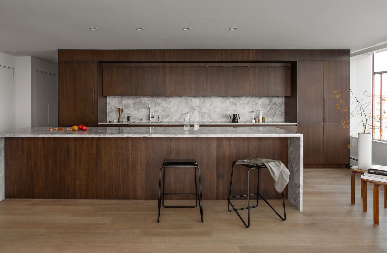 A kitchen with dark wooden cabinets and marble worktops