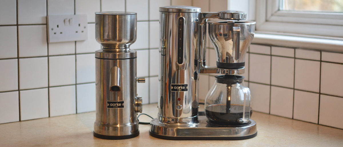 Image of the Aarke Coffee System – a stainless steel coffee bean grinder and drip coffee maker – positioned on a kitchen counter