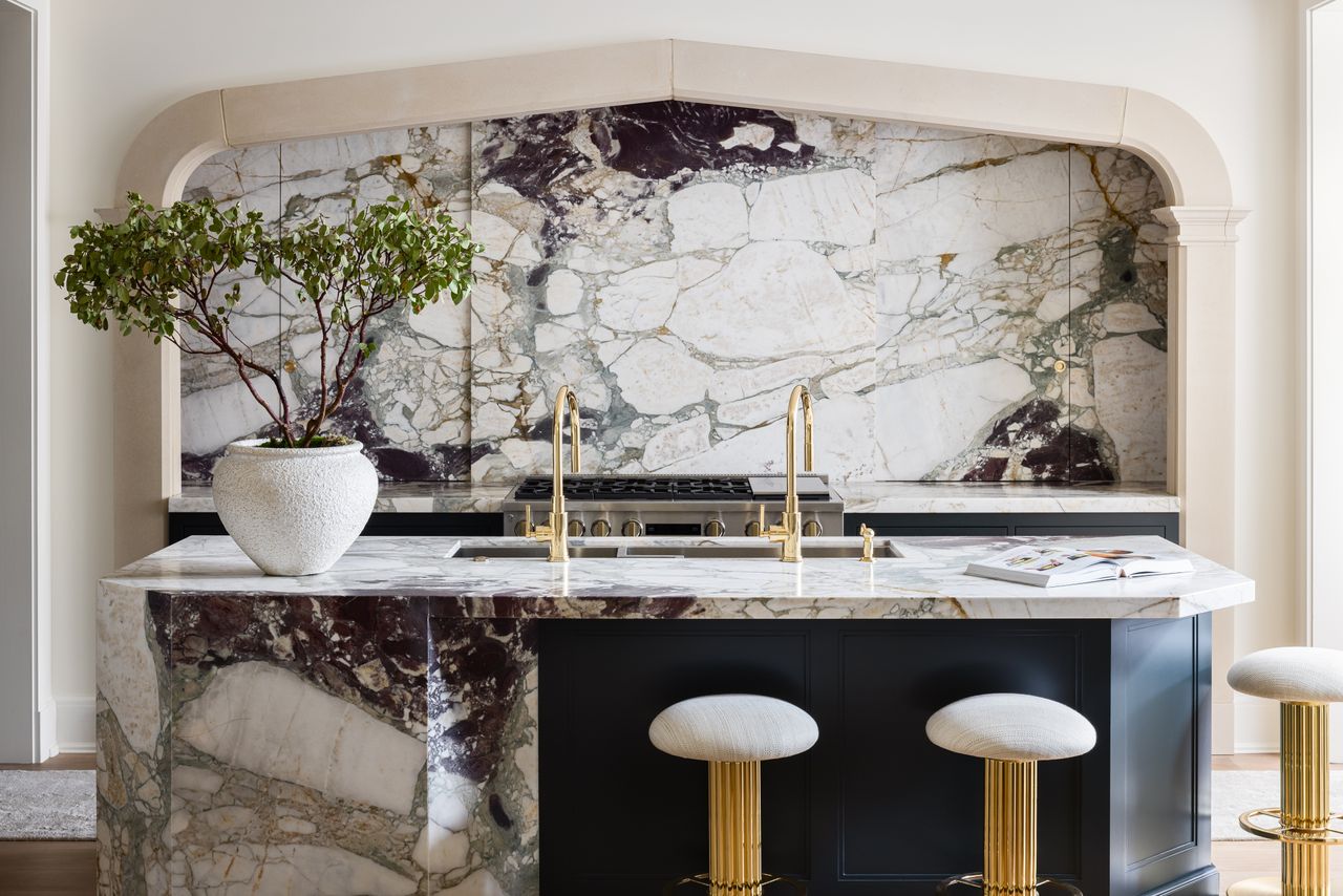 A kitchen with marble, veined backsplash and gold hardware