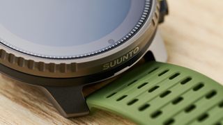 a super close up shot on the bezel of an outdoor-style smartwatch with a big screen and titanium bezel case with a forest green strap