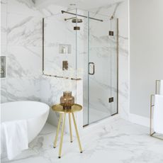grey and white marble tiled bathroom with white freestanding bath and shower cubicle with glass screen and door, brass fittings