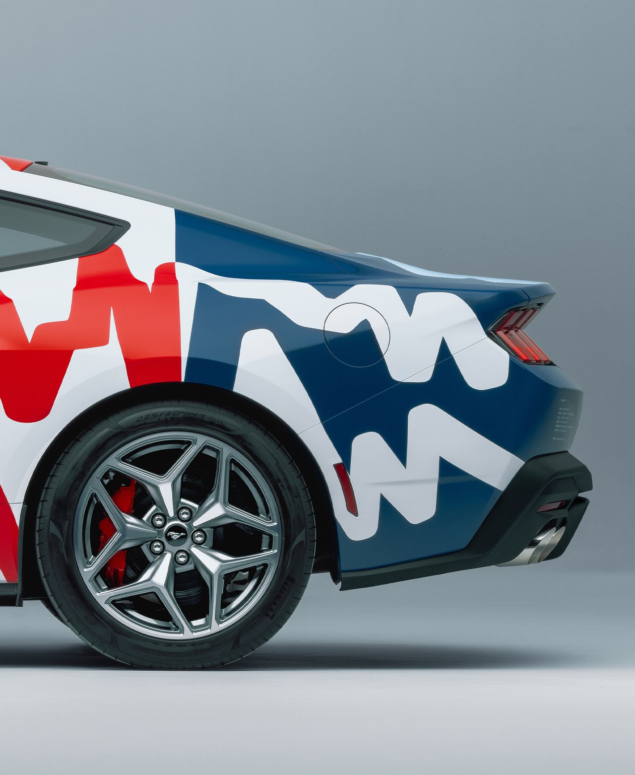 Photograph of the 60th year anniversary celebratory Mustang collaboration with Haus of Thrills. Close-up view from the side of the rear of the white Mustang with colourful lines in white, red and blue with an occasional blue background.