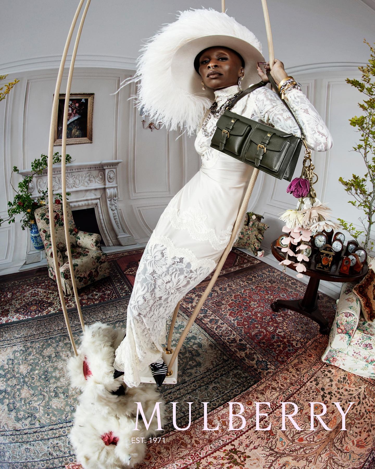 Cynthia Erivo wears a white dress, white feather had and carries Mulberry bag in green