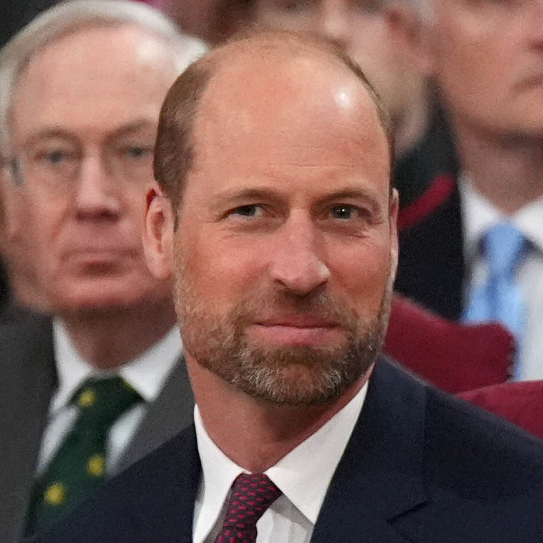 Prince William has a beard and a bald head and is smiling while wearing a navy suit and tie
