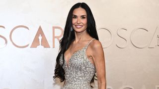 Demi Moore at the 2025 Oscars, smiling with long curled black hair and wearing a silver crystal-embellished gown