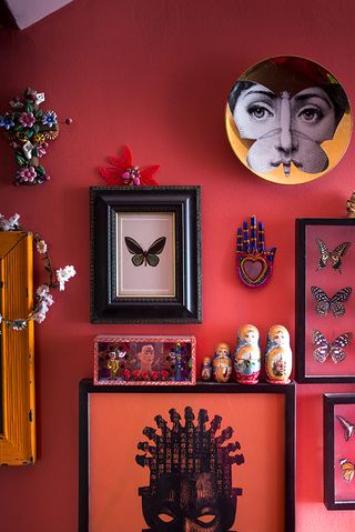 Red room with a gallery wall and a white and yellow fornasetti plate with a woman's face in the shape of a butterfly on it