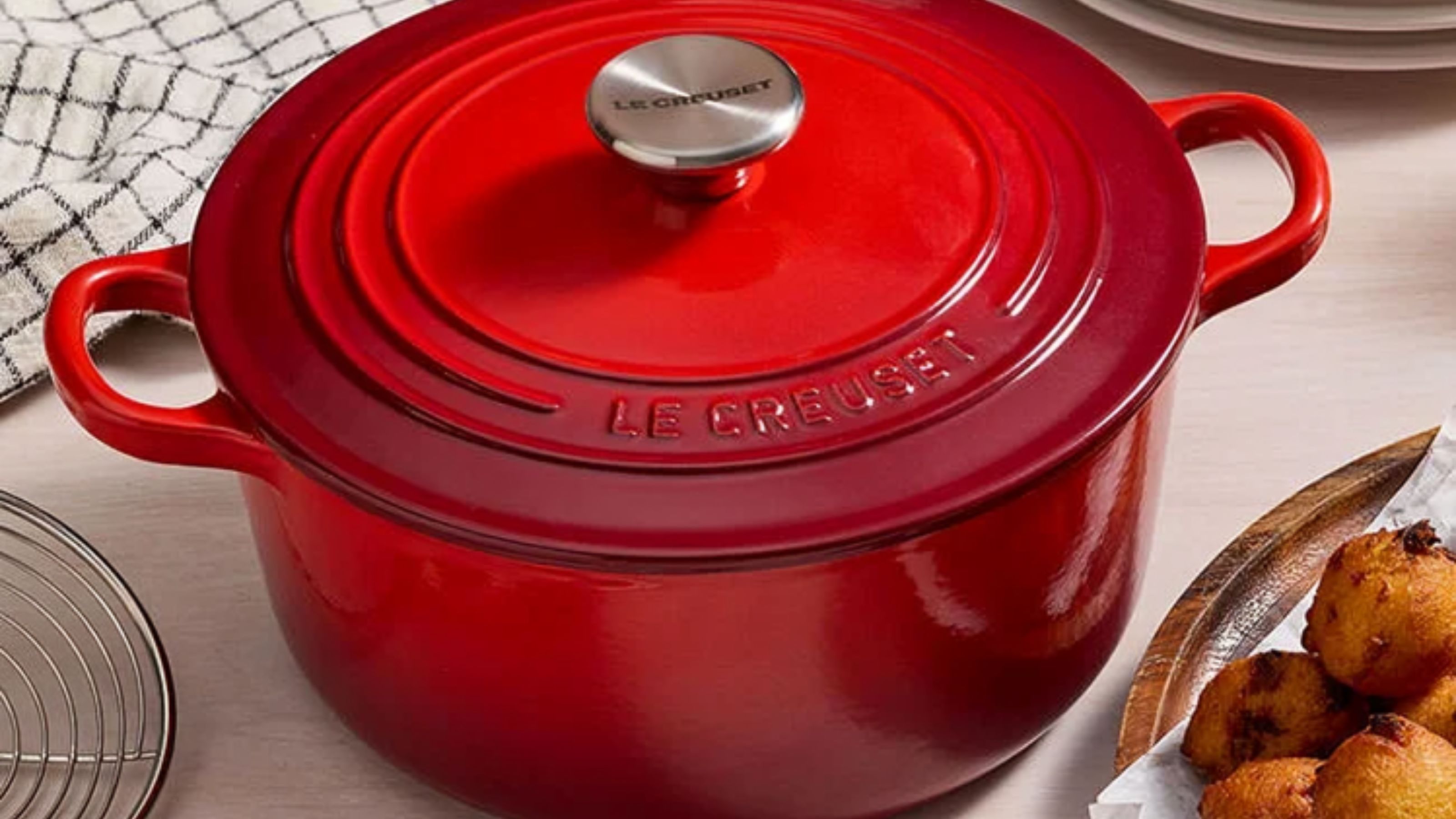 a red le Creuset Dutch Oven on a kitchen table, with a silver handle. 