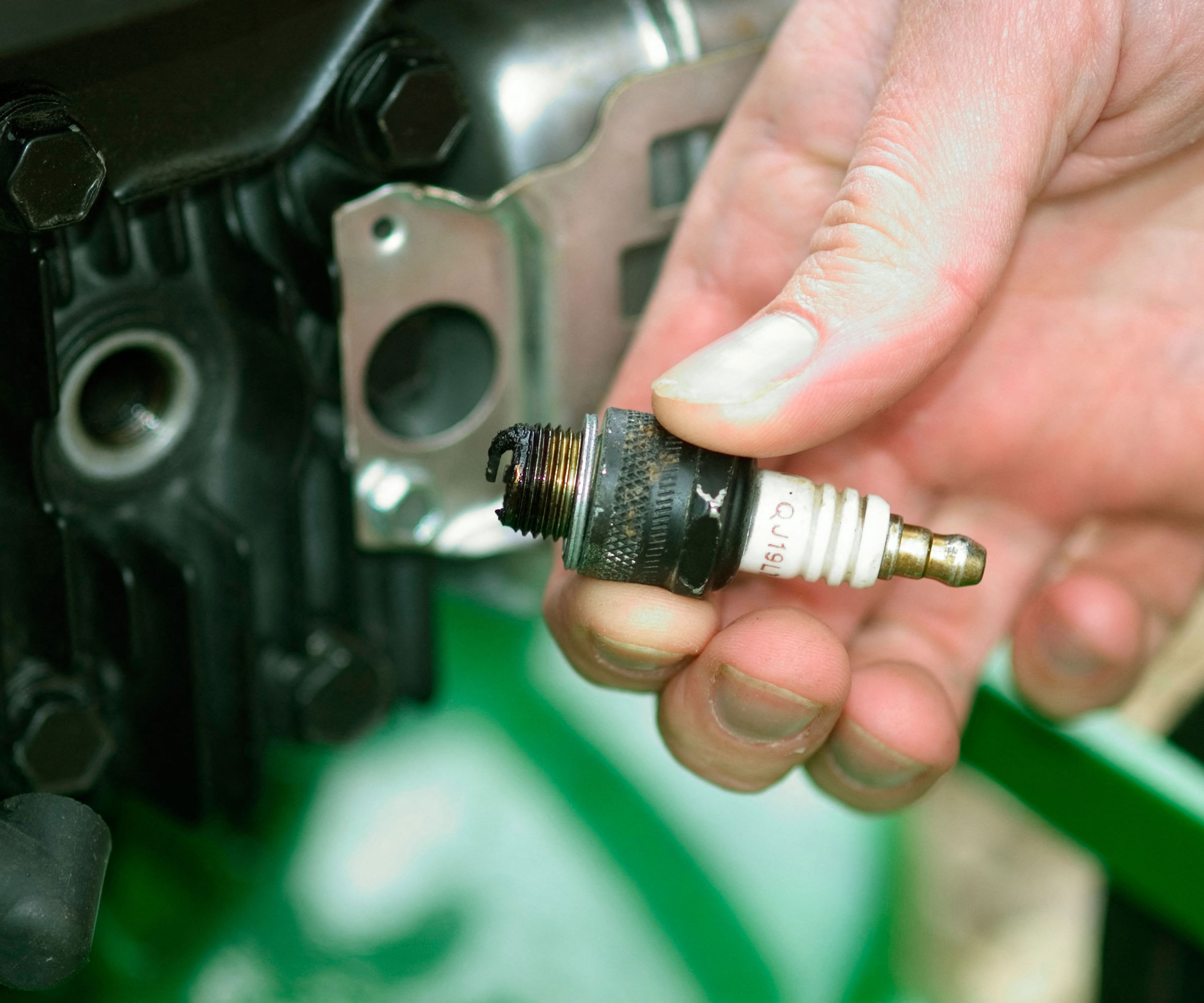 hand holding worn spark plug in front of green lawn mower