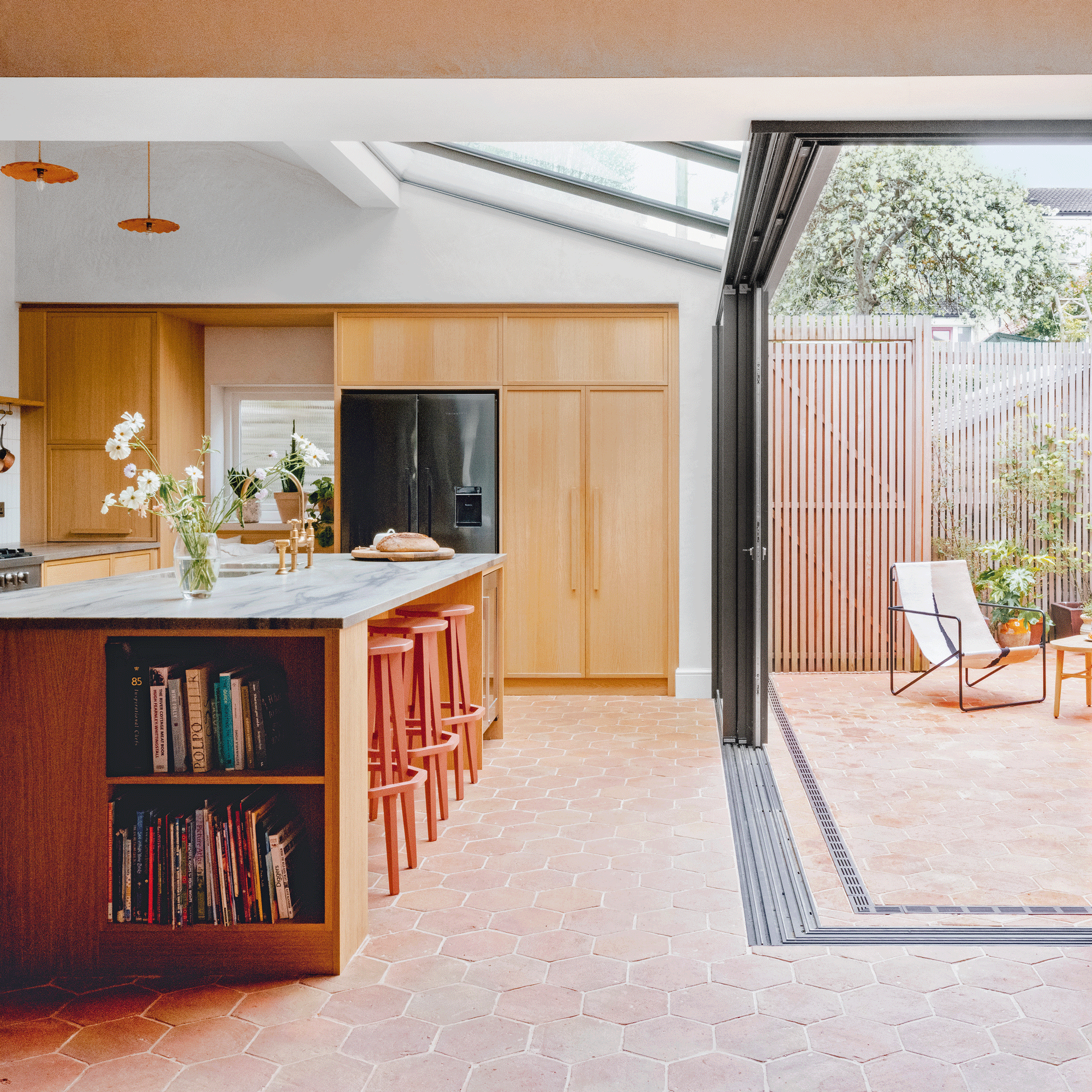 a wooden kitchen with tiled floor and large, sliding patio doors with a large fridge freezer and kitchen island with breakfast bar