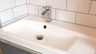 White bathroom snike with chrome monobloc tap and white metro tile background