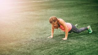 Woman performing burpee outdoors on grass