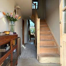 Hallway with wooden sideboard decorated with candle and vase of flowers beside unfinished staircase