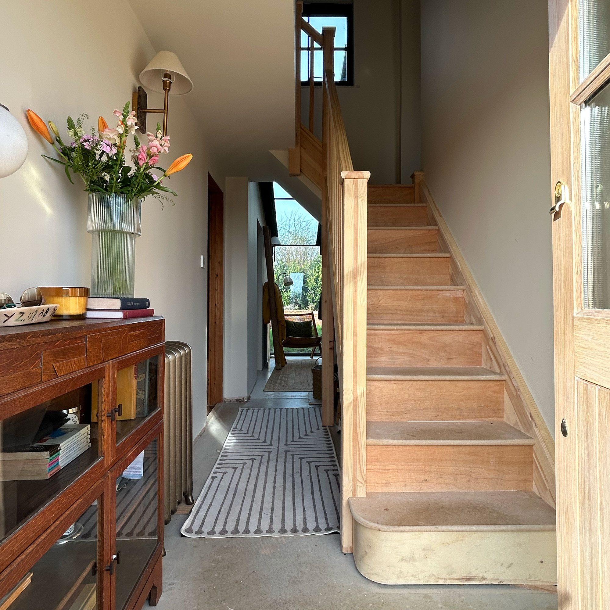 Hallway with wooden sideboard decorated with candle and vase of flowers beside unfinished staircase