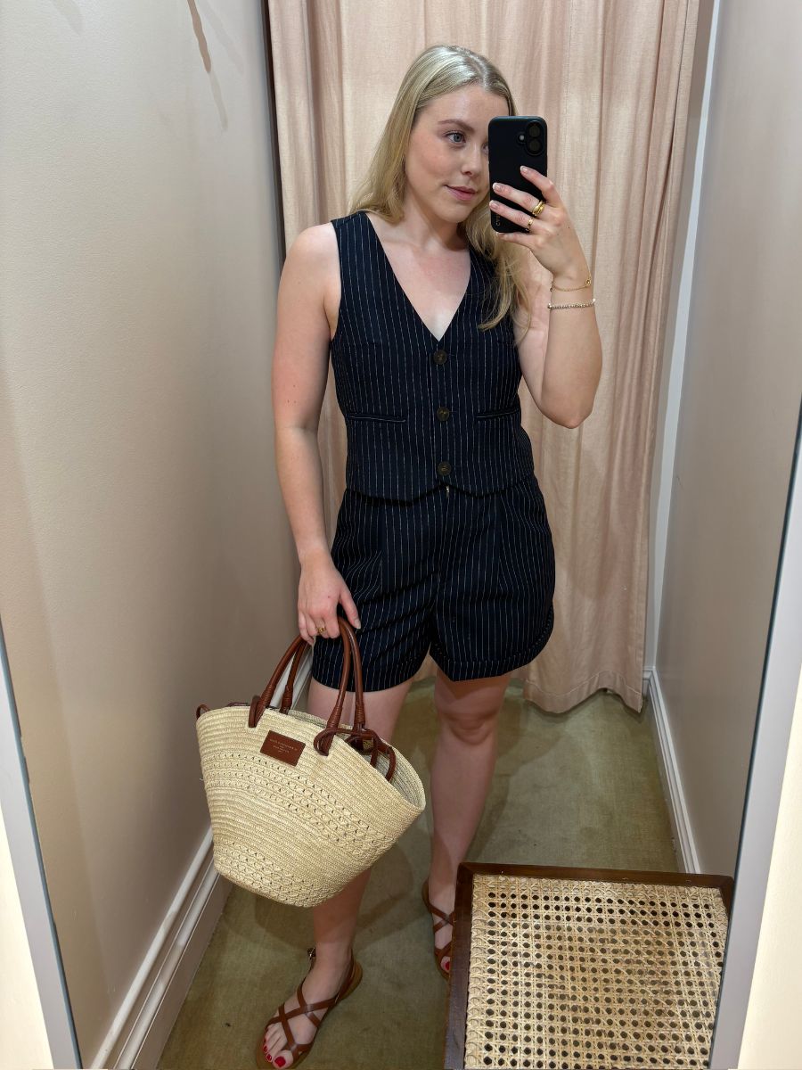 Woman wears matching pinstripe waistcoat and shorts, carries basket bag and sandals.