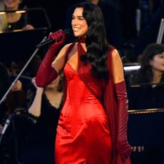 Dua Lipa wears a red galliano dress with her new black hair onstage at a london performance