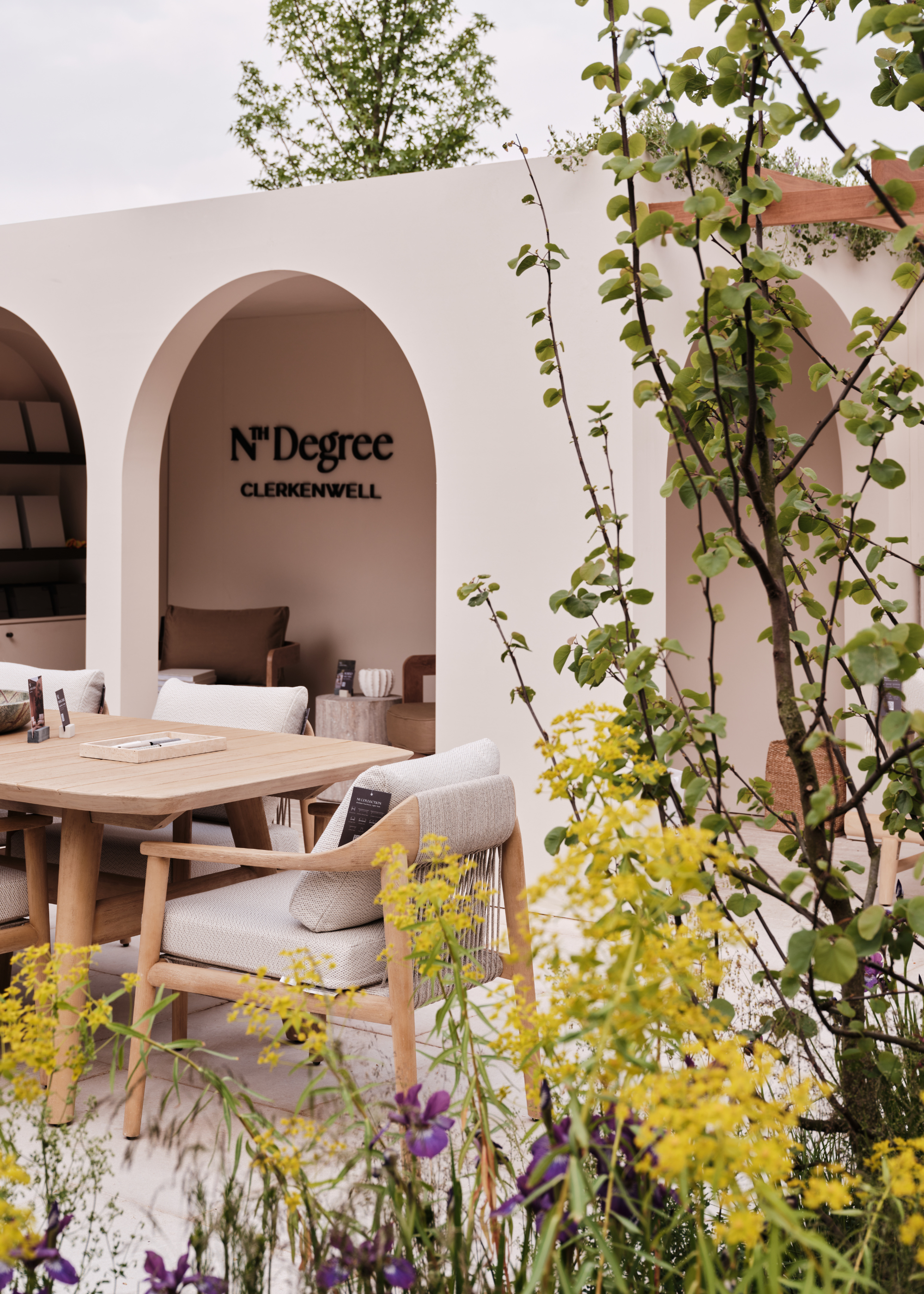 A still from Nth Degree's exhibit at the 2025 Chelsea Flower Show featuring an outdoor dining space beside a container garden of colorful flowers and green foliage