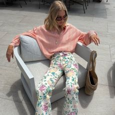 Model @hoskelsa sits on an armchair wearing floral high-waisted jeans with suede sandals and a peach lightweight knit.