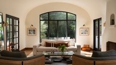 A modern living room with an arched window alcove, two cane chairs, and a cream sofa