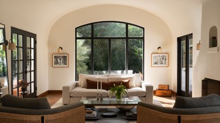 A modern living room with an arched window alcove, two cane chairs, and a cream sofa