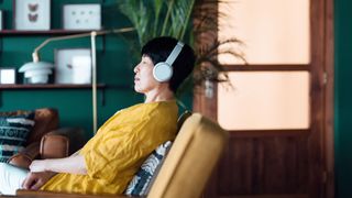 Woman sitting on armchair with eyes closed listening to music and smiling