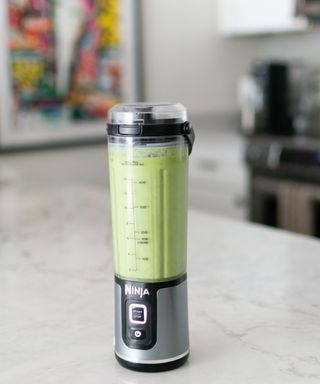 A portrait shot of the Ninja Blast portable blender in Heather Biens kitchen on white marble worktop with green smoothie drink