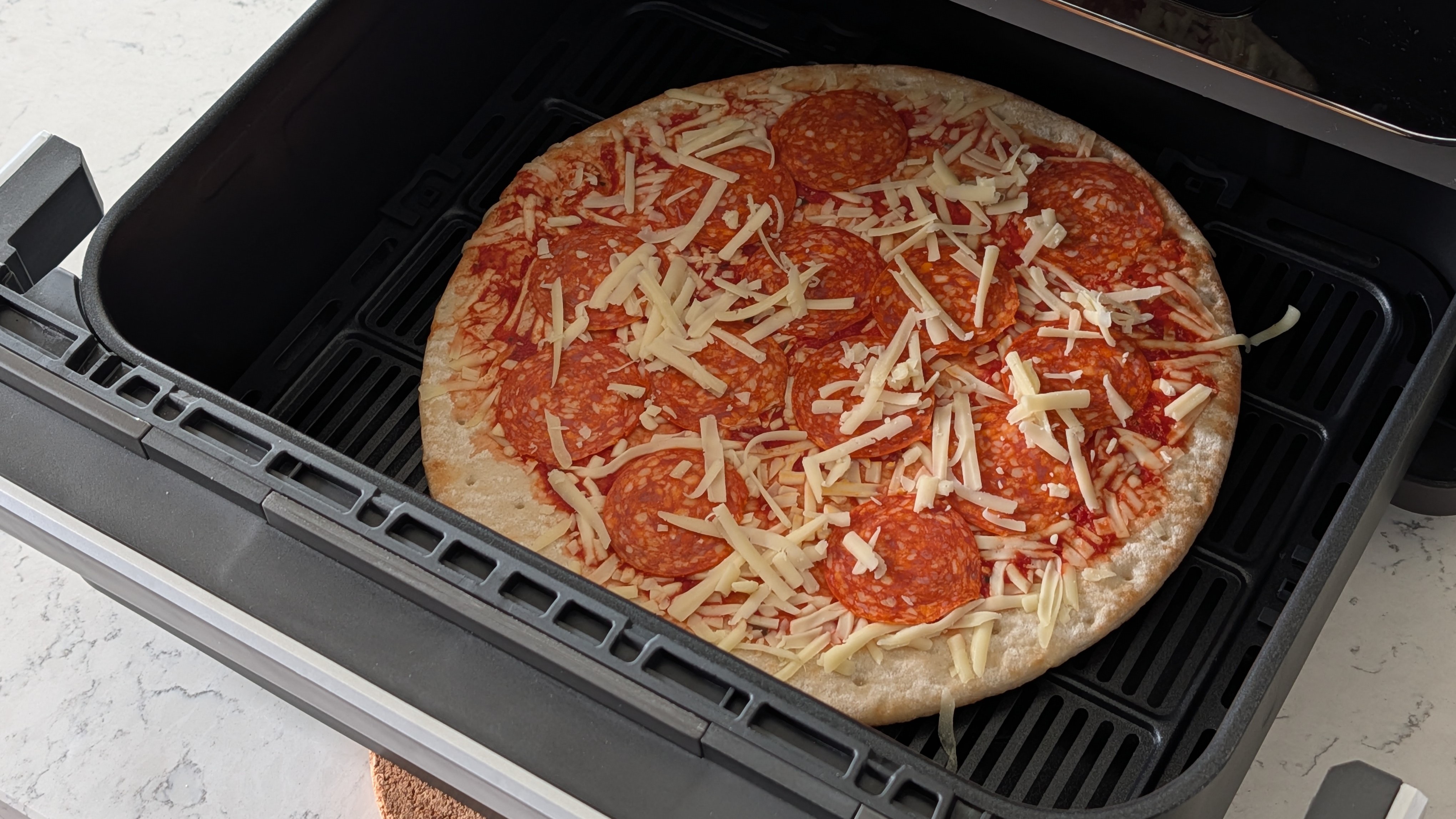 Uncooked pizza in air fryer drawer