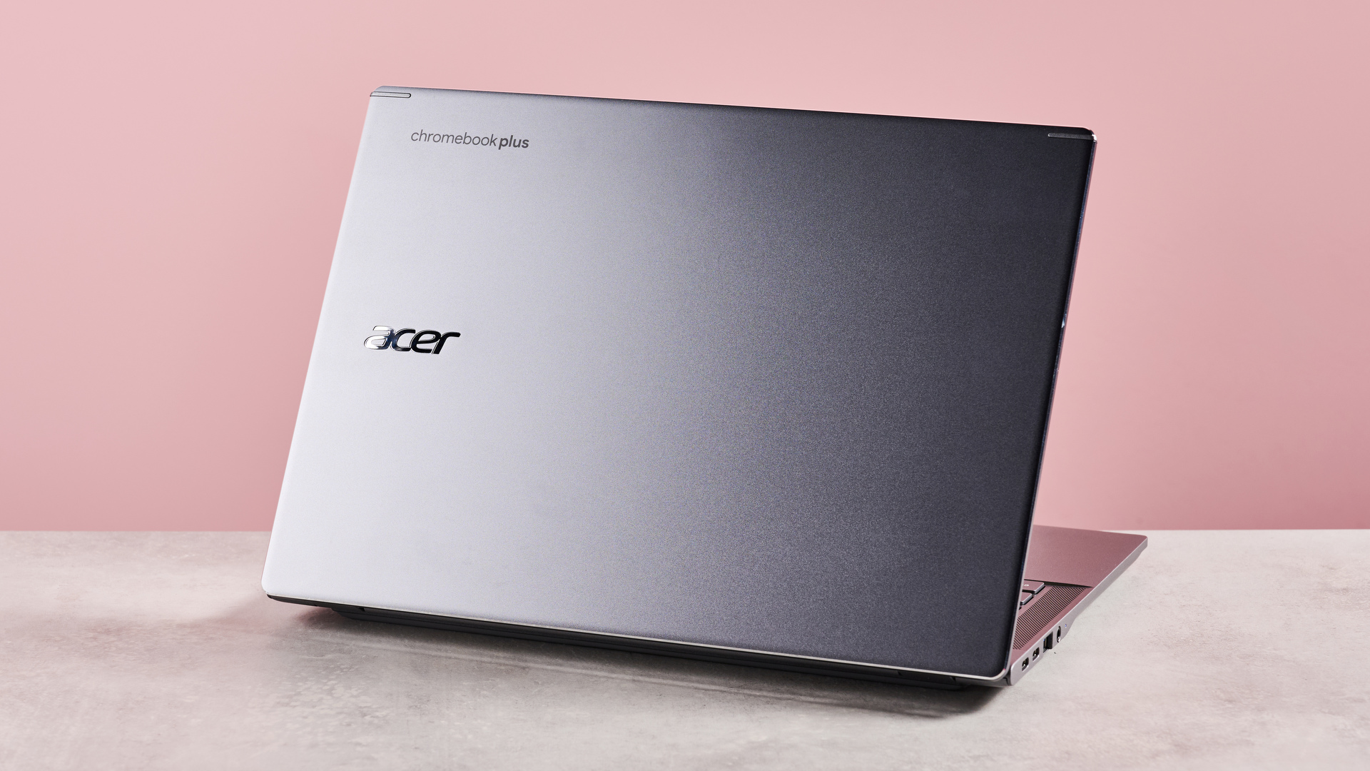 Back of Acer Chromebook Plus 516 open on desk with pink background