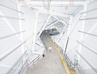 Interior view of The Twist by Bjarke Ingels Group (BIG) during the construction phase. The twisted structure is white inside and construction staff can be seen along with a long yellow tube