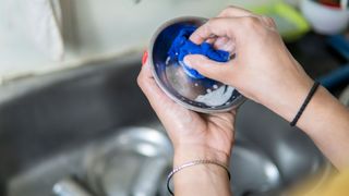 A person washing a stainless steel cat bowl