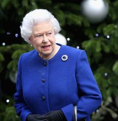 Queen Elizabeth in a blue coat standing in front of a Christmas tree
