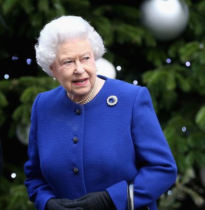 Queen Elizabeth in a blue coat standing in front of a Christmas tree