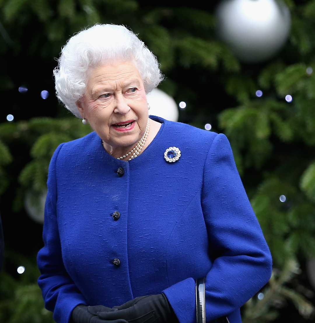 Queen Elizabeth in a blue coat standing in front of a Christmas tree