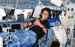 Sally K. Ride 'floating' in microgravity surrounded by papers and equipment.